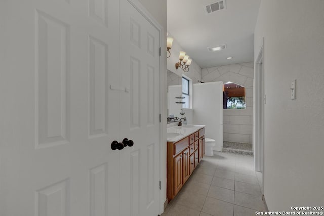 bathroom with a tile shower, tile patterned flooring, vanity, and toilet