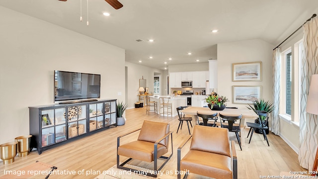 living room featuring ceiling fan, light hardwood / wood-style floors, and vaulted ceiling