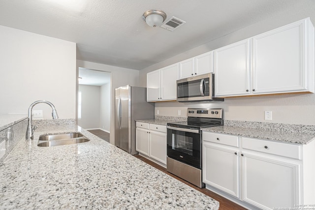 kitchen with white cabinets, stainless steel appliances, light stone countertops, and sink