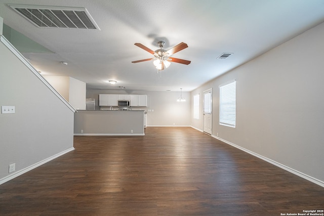 unfurnished living room featuring dark hardwood / wood-style flooring and ceiling fan with notable chandelier