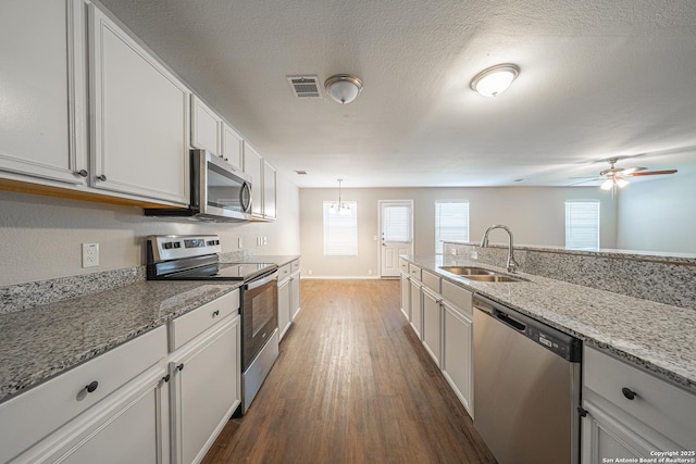 kitchen featuring sink, stainless steel appliances, light stone counters, decorative light fixtures, and white cabinets