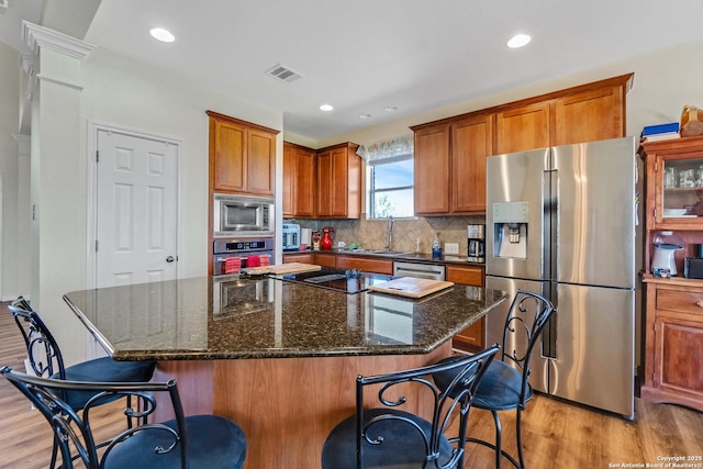 kitchen with a kitchen breakfast bar, tasteful backsplash, stainless steel appliances, light hardwood / wood-style floors, and a kitchen island