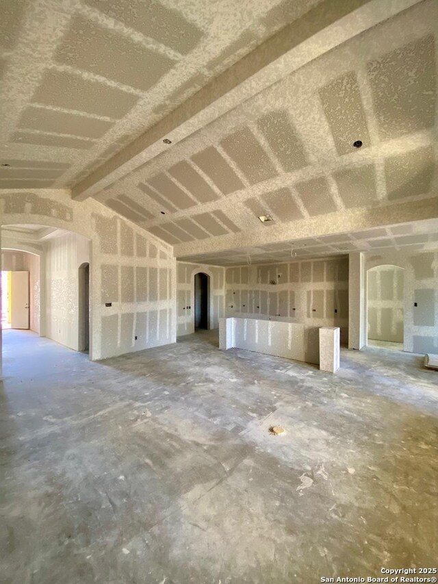 unfurnished living room with arched walkways and vaulted ceiling