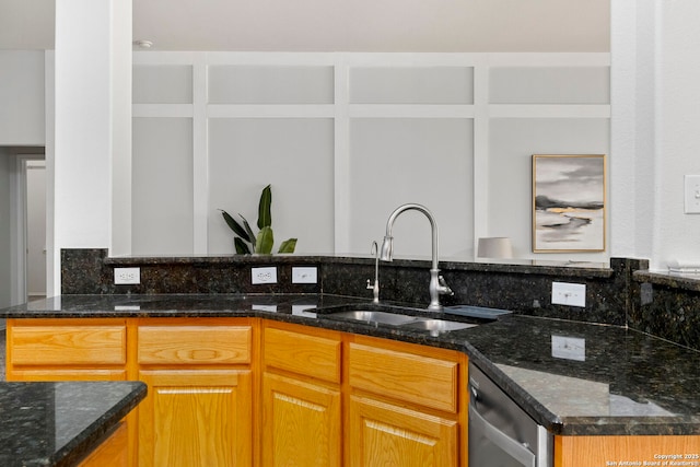 kitchen featuring stainless steel dishwasher, dark stone countertops, and sink