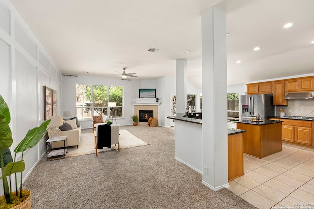 kitchen with ceiling fan, backsplash, light colored carpet, a kitchen island, and appliances with stainless steel finishes