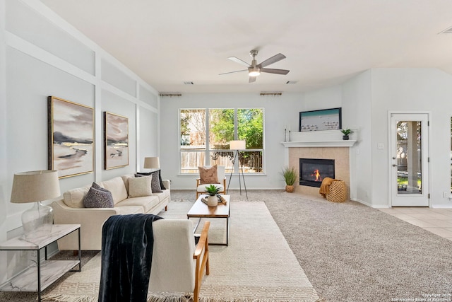 living room with a tile fireplace, light carpet, and ceiling fan