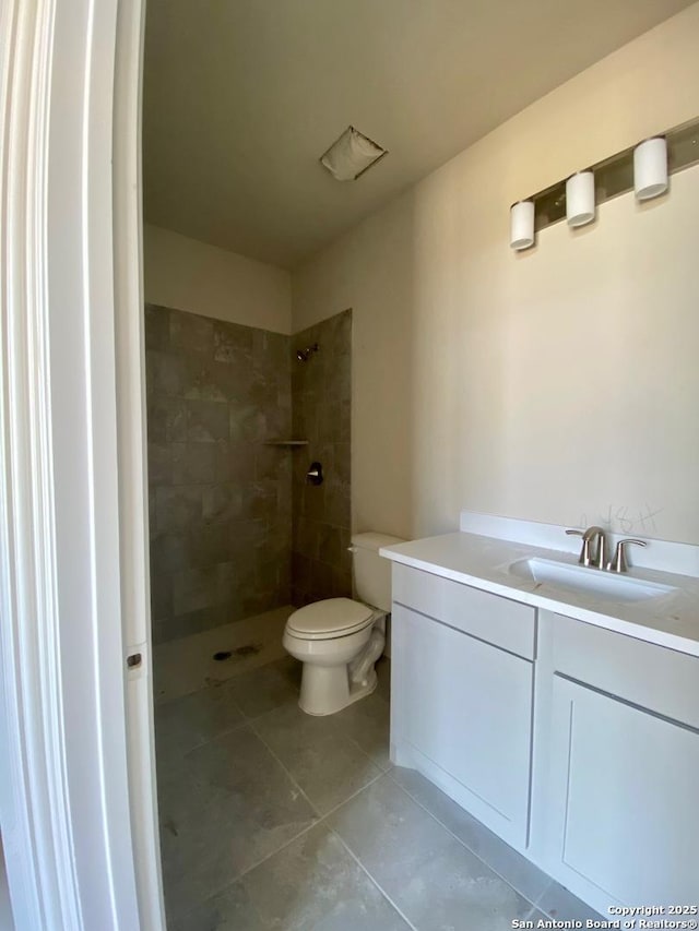 bathroom with a tile shower, tile patterned flooring, vanity, and toilet