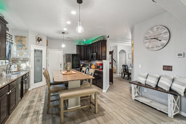 kitchen with sink, hanging light fixtures, stainless steel appliances, light stone counters, and dark brown cabinets