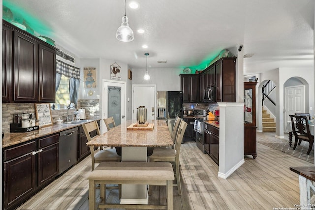 kitchen featuring stainless steel appliances, light hardwood / wood-style flooring, pendant lighting, dark brown cabinets, and a kitchen island