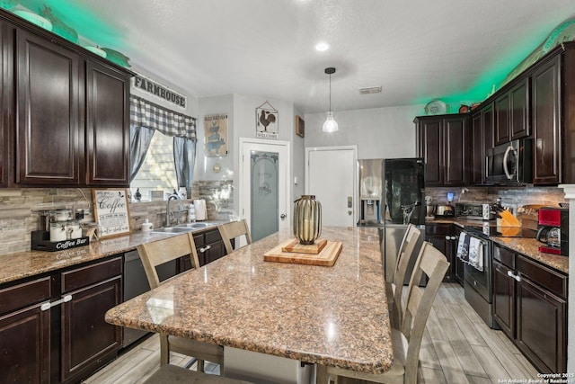 kitchen with hanging light fixtures, backsplash, a breakfast bar area, a kitchen island, and appliances with stainless steel finishes