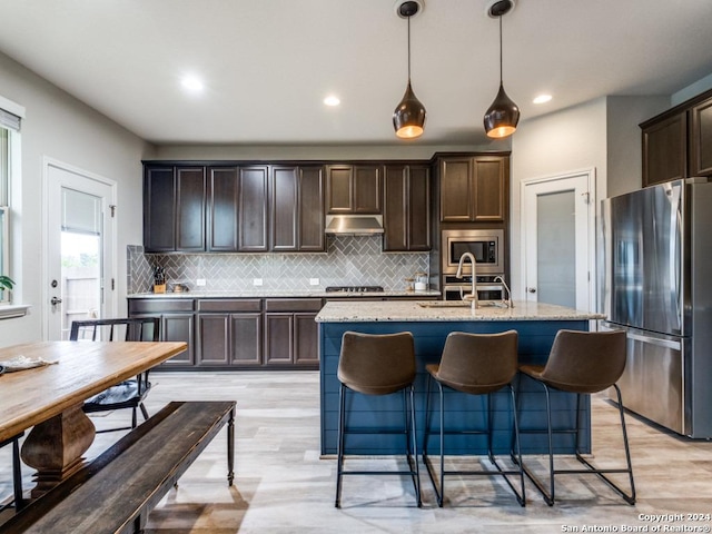 kitchen featuring pendant lighting, sink, light stone countertops, an island with sink, and appliances with stainless steel finishes