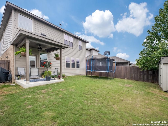 rear view of property featuring ceiling fan, a trampoline, a patio, and a yard