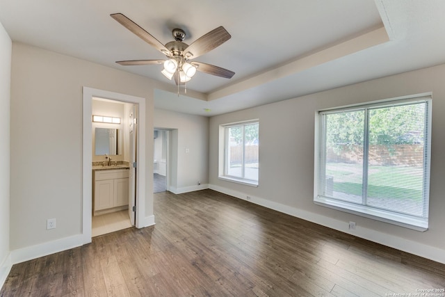 unfurnished bedroom featuring hardwood / wood-style floors, ceiling fan, a raised ceiling, and ensuite bath