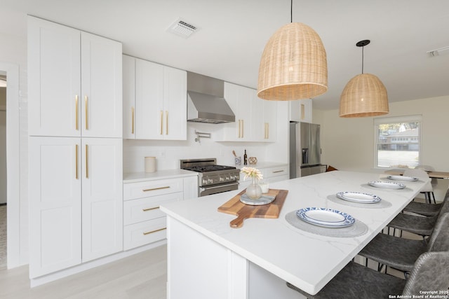 kitchen featuring white cabinetry, hanging light fixtures, stainless steel appliances, wall chimney range hood, and a breakfast bar