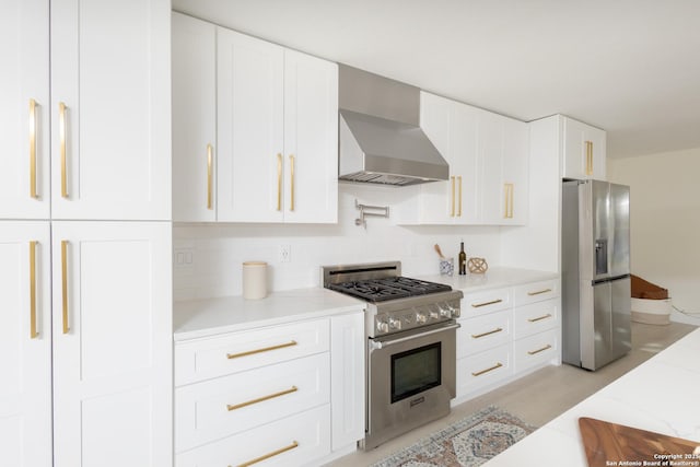 kitchen featuring appliances with stainless steel finishes, white cabinetry, and wall chimney range hood