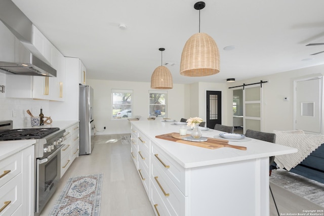 kitchen featuring a center island, white cabinets, wall chimney range hood, a barn door, and stainless steel appliances