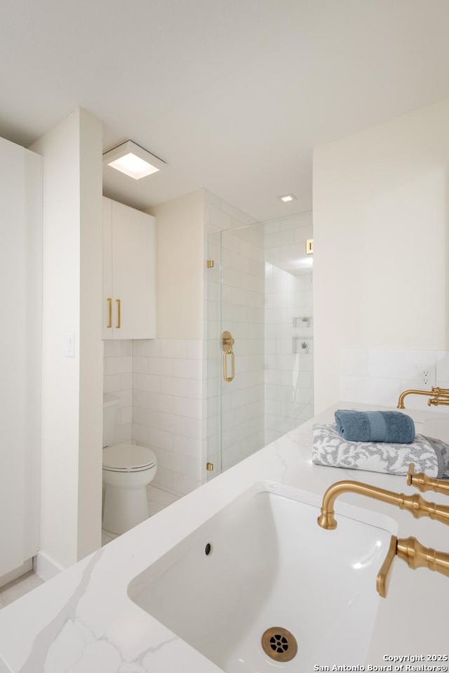 bathroom with a shower with door, vanity, tile walls, and toilet