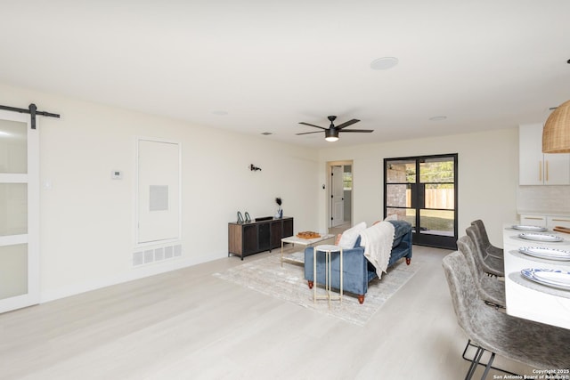 living room featuring a barn door, light hardwood / wood-style floors, and ceiling fan