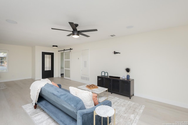 living room with a barn door, light hardwood / wood-style floors, and ceiling fan