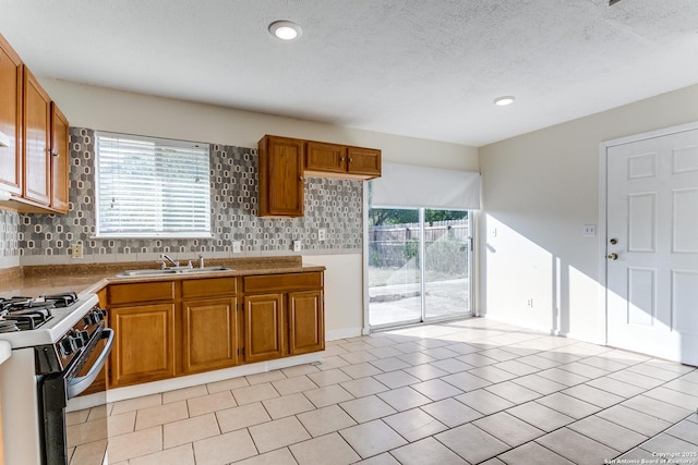 kitchen featuring tasteful backsplash, a textured ceiling, gas stove, sink, and light tile patterned flooring