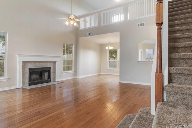 unfurnished living room with a tile fireplace, hardwood / wood-style floors, ceiling fan with notable chandelier, and a high ceiling