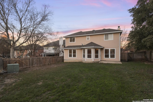 back house at dusk with a lawn and a patio area