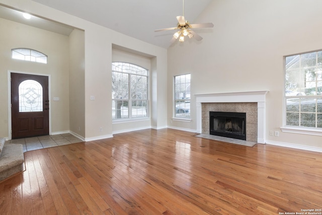 unfurnished living room with ceiling fan, light wood-type flooring, high vaulted ceiling, and a tiled fireplace