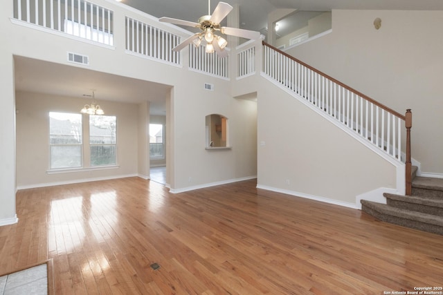 unfurnished living room with ceiling fan with notable chandelier, wood-type flooring, and a towering ceiling