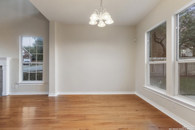 unfurnished dining area with a tiled fireplace, light wood-type flooring, and a notable chandelier