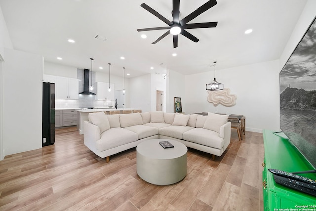 living room with ceiling fan with notable chandelier and light hardwood / wood-style floors