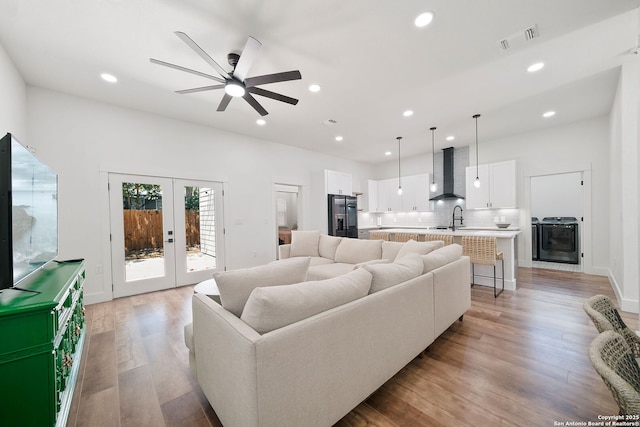 living room featuring french doors, light hardwood / wood-style floors, ceiling fan, sink, and washer / clothes dryer