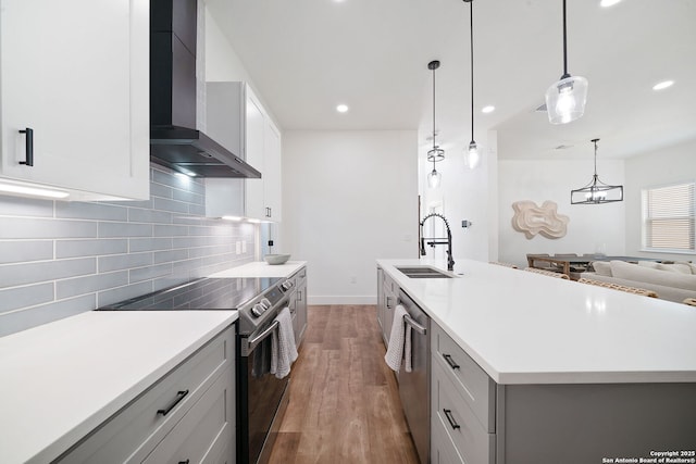 kitchen with sink, wall chimney range hood, pendant lighting, a spacious island, and appliances with stainless steel finishes