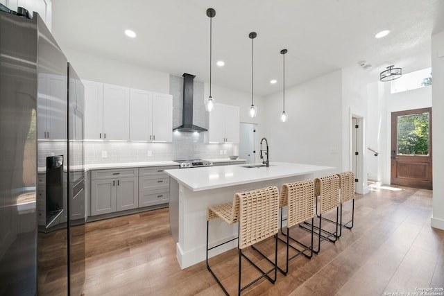 kitchen featuring a kitchen island with sink, a kitchen breakfast bar, wall chimney range hood, sink, and decorative light fixtures