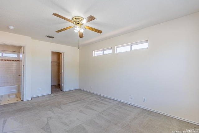 unfurnished bedroom featuring light carpet, a walk in closet, ensuite bathroom, ceiling fan, and a closet