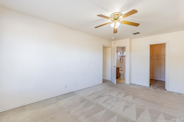 unfurnished bedroom featuring ceiling fan, light colored carpet, a walk in closet, and ensuite bath