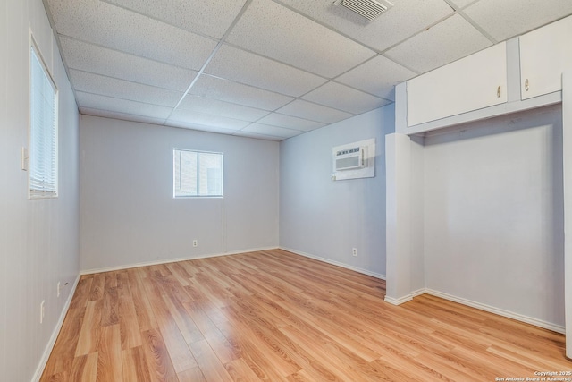 interior space with an AC wall unit, a paneled ceiling, and light wood-type flooring