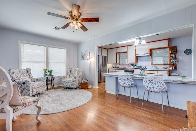 kitchen with a kitchen breakfast bar, ceiling fan, light wood-type flooring, kitchen peninsula, and stainless steel refrigerator