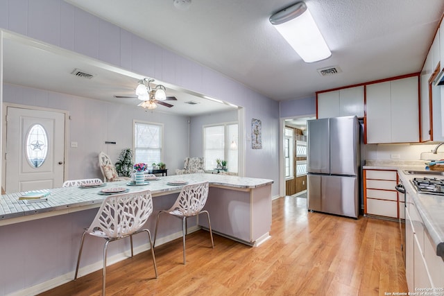 kitchen featuring ceiling fan, kitchen peninsula, light hardwood / wood-style floors, white cabinets, and appliances with stainless steel finishes