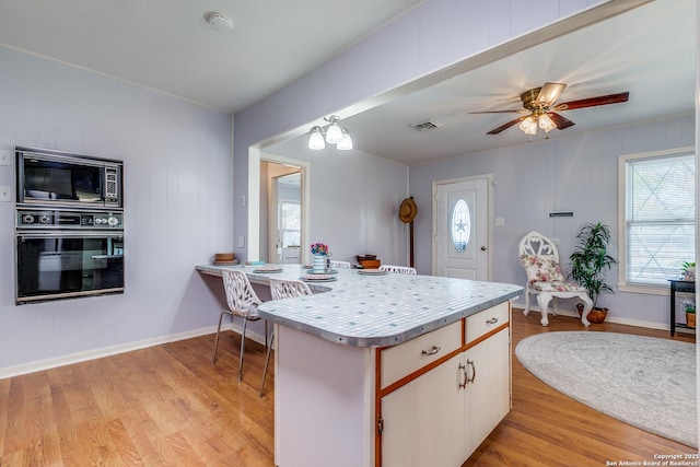 kitchen with black appliances, ceiling fan with notable chandelier, white cabinetry, and light wood-type flooring