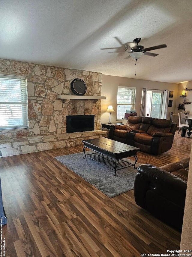 living room featuring a textured ceiling, a stone fireplace, ceiling fan, and dark hardwood / wood-style floors