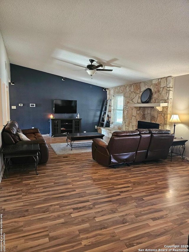 living room with dark hardwood / wood-style floors, ceiling fan, a stone fireplace, and a textured ceiling