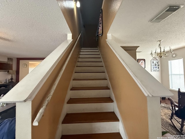 stairway featuring a textured ceiling and a chandelier