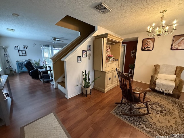 living room featuring dark hardwood / wood-style floors, ceiling fan with notable chandelier, and a textured ceiling