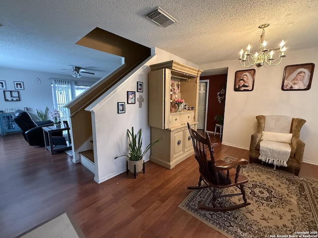 living area featuring dark hardwood / wood-style flooring, ceiling fan with notable chandelier, and a textured ceiling