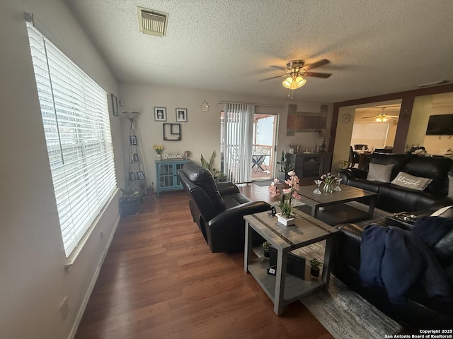 living room with a textured ceiling, ceiling fan, a healthy amount of sunlight, and dark wood-type flooring