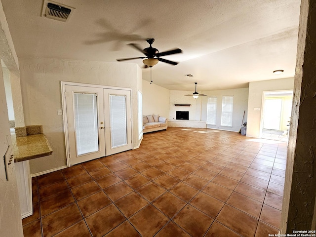 unfurnished living room with french doors, a brick fireplace, tile patterned flooring, ceiling fan, and a textured ceiling