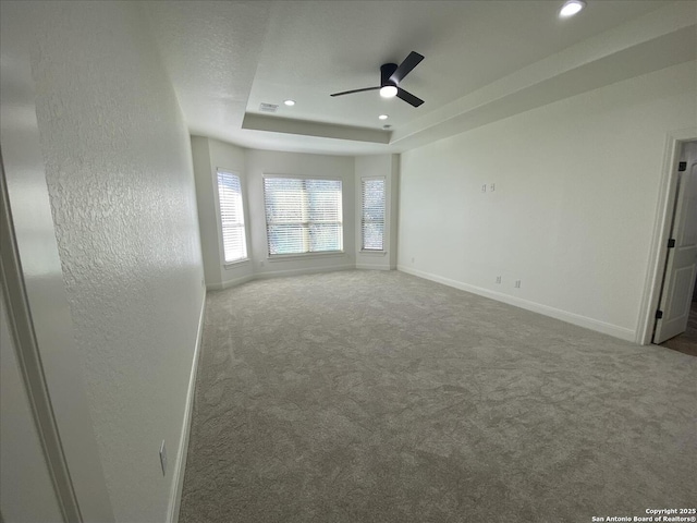 carpeted spare room with a tray ceiling and ceiling fan