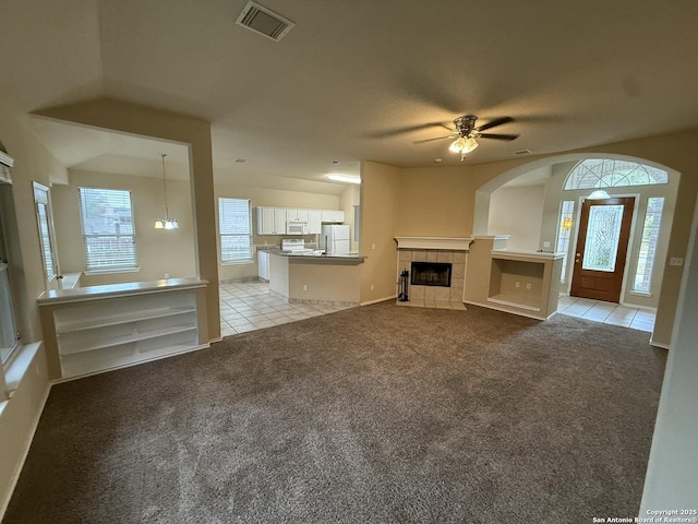 unfurnished living room with ceiling fan with notable chandelier, lofted ceiling, light carpet, and a tiled fireplace