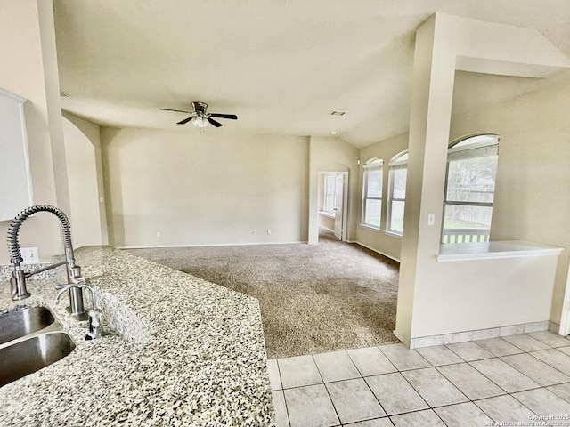 kitchen featuring ceiling fan, sink, light stone counters, vaulted ceiling, and light carpet