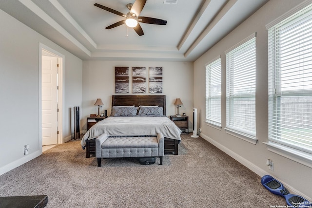 carpeted bedroom with a raised ceiling and ceiling fan